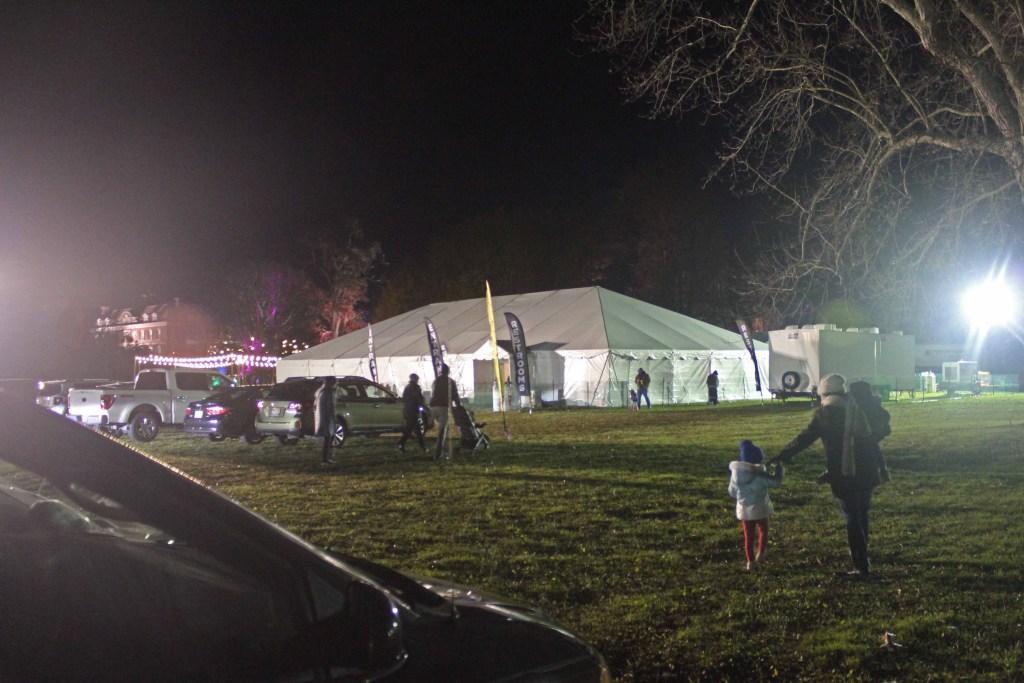 White tent in green grass field with cars parked nearby
